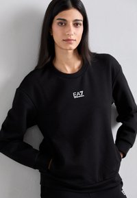 Felpa nera con scollo tondo, maniche lunghe e un piccolo logo EA7 bianco sul petto. Tessuto morbido e vestibilità comoda.