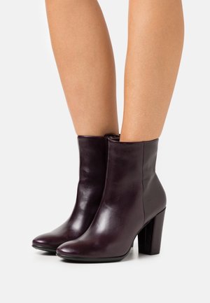 Bottes chevilles en cuir violet foncé avec une finition lisse, bout rond et un talon épais et haut, dotées d'une fermeture éclair sur le côté.