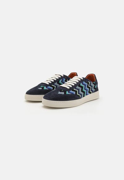 Mörkblå mocka sneakers med ett zigzag-mönster i grönt och blått, med krämfärgade snören och en ljusgummisula.