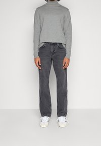 Maglione girocollo grigio a maglia abbinato a jeans dritti grigio scuro e sneakers bianche, con un tessuto strutturato e una vestibilità casual.