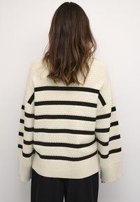 Cremfarbener Pullover mit schwarzen horizontalen Streifen, strukturiertem Strickmuster, gerippten Bündchen und Saum sowie einer lockeren Passform, von hinten gesehen.