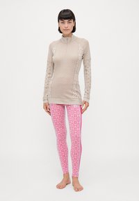 Beige mønstrete langermet topp med høy krage, kombinert med tettsittende rosa leggings med geometrisk design og rosa striper på sidene.
