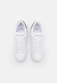 White sneakers featuring a textured upper, round toes, and flat laces. Includes branding on the tongue and heel. Sole is smooth and minimalist.