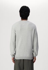 Pull en tricot côtelé gris clair avec des manches longues, un col rond et des poignets ajustés. La texture du tissu est douce avec des rayures horizontales.