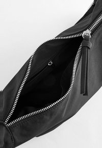 Zwarte stoffen tas met metalen rits, voorzien van een gladde textuur en een binnenzak. De ritsenfanaat heeft een decoratieve lintaccent.