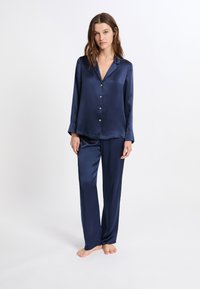 Conjunto de pijama de satén azul marino con camisa de manga larga abotonada y pantalones a juego; textura suave, ajuste relajado y brillo sutil en toda la prenda.