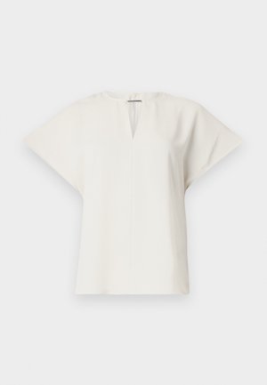 Kortermet hvit topp med V-hals og avslappet silhuett. Glatt stoff med subtil glans og sidesplitter for bedre bevegelighet.