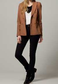 Brun dobbeltknappet blazer med guldknapper, parret med en sort top og sorte skinny jeans, afsluttet med sorte ankelstøvler.