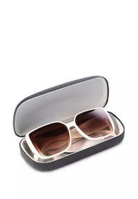 Białe, oversize okulary przeciwsłoneczne w czarnym, teksturowanym etui. Okulary mają brązowe soczewki w gradientowym kolorze oraz miękką podszewkę wewnętrzną. W zestawie ściereczka do czyszczenia.