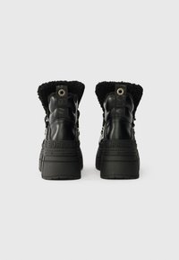 Mustad musta nahast platvormisaapad, millel on karvane must fliis, tekstuuriga tagapaneel, silmapaistev logo ja tugev kummist tald.