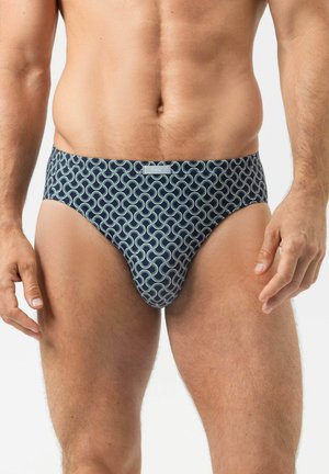 Männlicher Oberkörper, der marineblaue Unterhosen mit hellblauem, ineinandergreifendem Wirbelmuster vor weißem Hintergrund trägt.