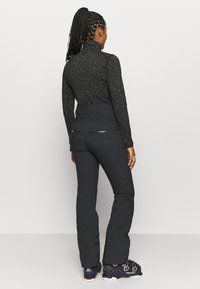 Musta vetoketjulla varustettu yläosa, jossa on teksturoitu kuvio ja korkea kaulus, yhdistetty mustiin housuihin, joissa on sivuvetoketjut ja vartalonmyötäinen leikkaus.