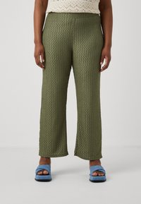 Green, textured wide-leg trousers with a diamond pattern, featuring an elastic waistband, paired with light blue slip-on sandals.