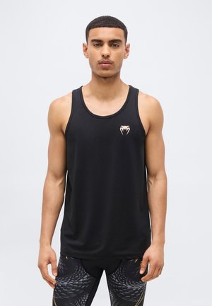 Junger Mann trägt ein schwarzes ärmelloses Sporttop mit einem kleinen Schlangenlogo auf der Brust und gemusterte schwarze Leggings mit Schuppenmuster.