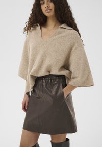 Pull en maille beige à col en V et manches courtes, associé à une jupe en similicuir brun foncé avec une taille élastique et des poches.