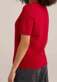 Czerwony krótki sweter z dzianiny o fakturze, z ribbowanym kołnierzem i dołem, dopasowany kształt oraz subtelne pionowe wzory.