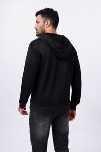 Un hoodie noir avec une texture douce, doté d'une capuche à cordon de serrage, de manches longues et d'un ourlet côtelé, associé à un jean en denim sombre.