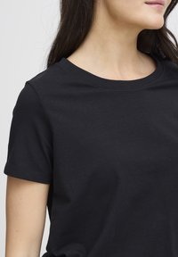 Fekete rövid ujjú póló puha pamutból, klasszikus kerek nyakkivágással és sima textúrával, közelről bemutatva.