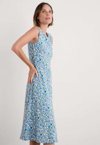 Kleita bez piedurknēm ar zilu ziedu rakstu, kurā ir zaļas un purpura akcenti, vidēja garuma, ziedu dizains ar maigu auduma tekstūru.