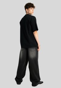 Przesadnie duża czarna koszulka bawełniana w luźnym kroju, w połączeniu z luźnymi czarnymi dżinsami o wyblakłym wykończeniu i dwiema tylnymi kieszeniami.