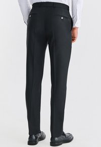 Czarne dopasowane spodnie o gładkiej tkaninie, z wąskim krojem, dwiema tylnymi kieszeniami i guzikami; noszone z czarnymi butami i białą koszulą.