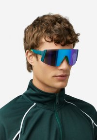 Zonnebril met grote, getinte, verloopglazen in blauw- en paarstinten. Smal groen plastic montuur met een hoekig ontwerp.