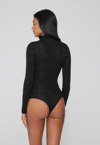 Body nero a maniche lunghe con design aderente, tessuto strutturato e fondo alto. Presenta un colletto alla coreana e dettagli minimi.