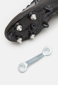 Scarpa da football nera con tacchetti metallici rimovibili accanto a una chiave inglese argento con logo Puma, aperture esagonali su entrambe le estremità.