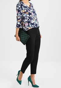 Blusa floreale blu navy con maniche a tre quarti, pantaloni neri a sigaretta, pochette verde trapuntata e décolleté turchesi.