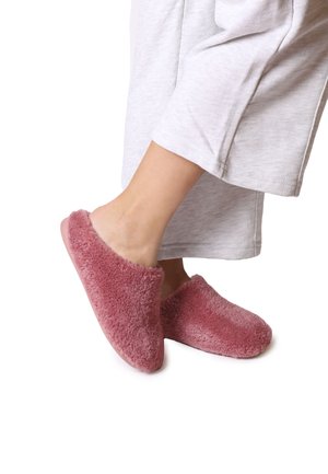 Zapatillas de casa rosas y esponjosas, hechas de un tejido suave y texturizado, con parte trasera abierta, combinadas con ropa de estar ligera de color gris claro y puños ligeramente arremangados.