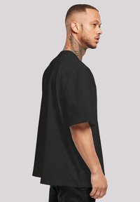 Černé oversized tričko s krátkými rukávy, vyrobené z bavlny. Má volný střih a čistý, jednoduchý design bez vzorů.