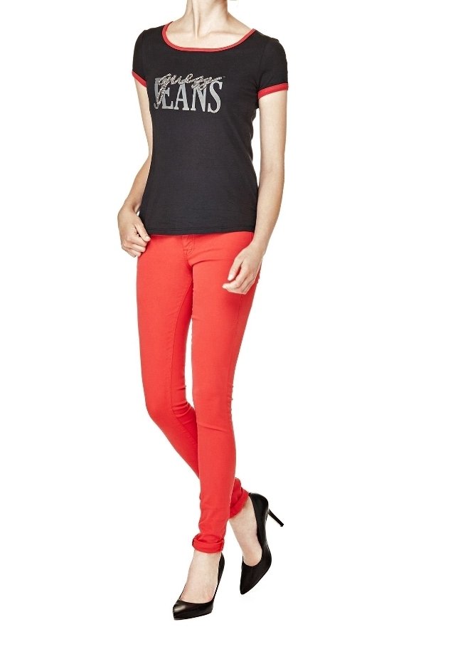 Femme portant un t-shirt noir ajusté avec une bordure rouge et un texte, un pantalon skinny rouge et des chaussures noires à talons hauts, debout avec une main dans la poche.