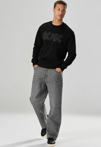 Fekete pulóver "AC/DC" logóval, texturált nyomattal, laza illesztésű szürke farmernadrággal és fekete sportcipővel párosítva.