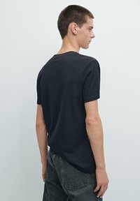 T-shirt nera a maniche corte con scollo rotondo e dettagli di cucitura visibili. Il tessuto appare morbido, strutturato e con un design casual.