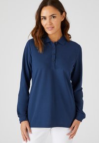 Marineblauwe poloshirt met lange mouwen, gemaakt van zachte stof, met een knoopsluiting en een ontspannen pasvorm, gecombineerd met witte broek.