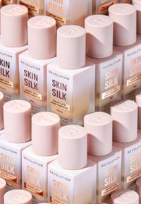 Revolution Skin Silk; firkantede flasker med lyserøde låg og klare bunde, der har guldmærkning og en glat mat finish.