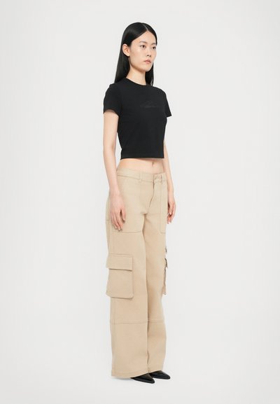 Black cropped t-shirt with a subtle logo, paired with beige cargo pants featuring multiple pockets and a loose fit, completing the outfit with black shoes.
