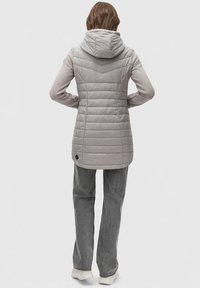 Lys grå, quilted jakke med hætte, som har et struktureret design, forlænget ryg og et lille logo-accent nær kanten. Sammen med grå bukser.