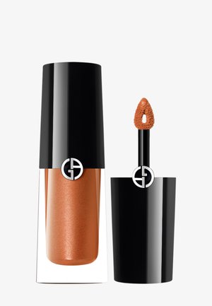 Rouge à lèvres liquide brillant dans un tube en verre transparent avec un capuchon noir. La couleur est un cuivre-orange métallique avec un applicateur en forme de pied de faon texturé.