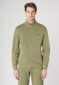 Giacca zip-up verde oliva realizzata in tessuto morbido, caratterizzata da un colletto alto, polsini e orlo a costine, con un piccolo logo sul lato sinistro del petto.