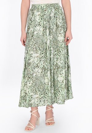 Nő zöld és bézs állatmintás redős midi szoknyában, rugalmas derékpánttal, bézs pántos magassarkú szandálban.
