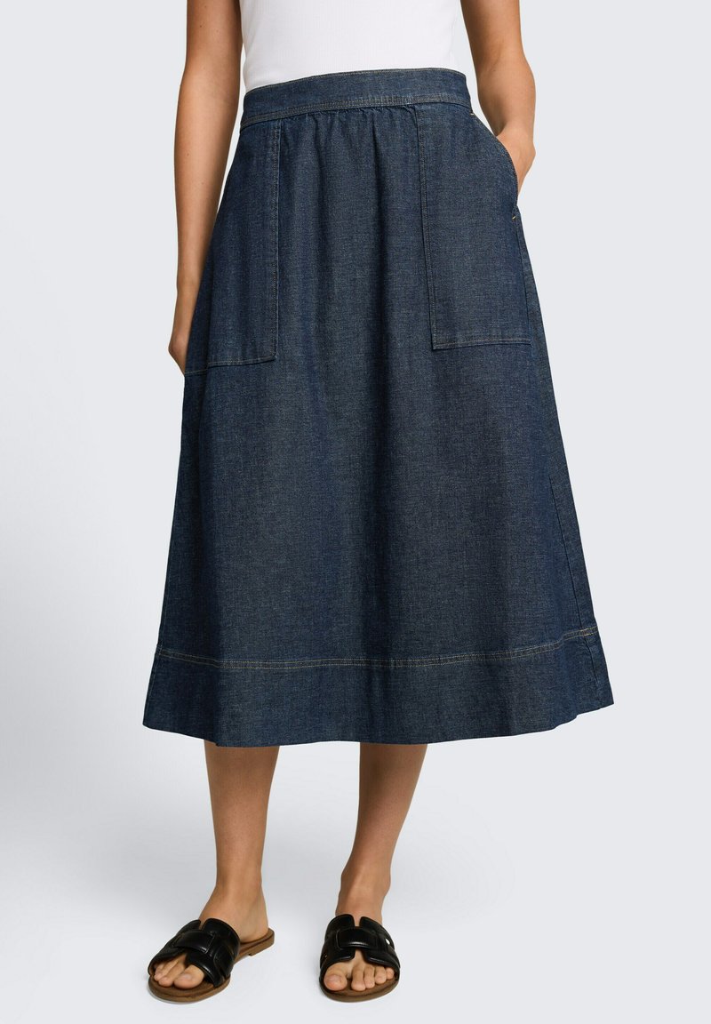 Woman wearing a dark blue denim midi skirt with large front pockets, paired with black open-toe slip-on sandals and a white top.