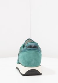 Chaussure de course en daim et maille teal avec un logo noir au talon, une semelle intermédiaire blanche et une semelle extérieure en caoutchouc texturé. Forme arrondie et col rembourré.