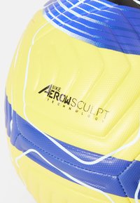 Pallone da calcio Nike con design esagonale in giallo e blu, superficie testurizzata e branding della tecnologia Aerowsculpt.