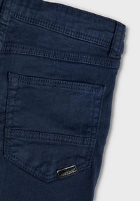 Marineblå denim jeans med en baklomme i rektangulær form, subtile sømdetaljer og en liten svart etikett som aksent.