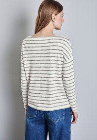 Gestreiftes langärmliges Oberteil in Creme mit grauen Horizontalstreifen, mit entspannter Passform und Rundhalsausschnitt. Kombiniert mit blauen Jeans.
