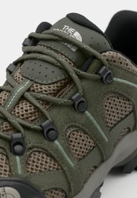 Zielone buty hikingowe z siateczkowymi i zamszowymi materiałami, z czarnymi akcentami, teksturowanym systemem sznurowania oraz logo na języku.