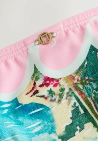 Gros plan sur un tissu rose avec un imprimé floral coloré et un petit pendentif en métal doré rond cousu près de la couture.