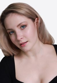 Collana choker argento con piccole perle rotonde, design della catena delicato, indossata su un top nero. Texture liscia con una lucentezza sottile.