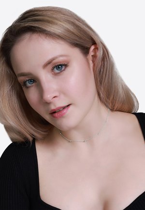 Silberne Choker-Halskette mit kleinen runden Perlen, filigranes Kettendesign, getragen über einem schwarzen Oberteil. Glatte Textur mit dezentem Glanz.